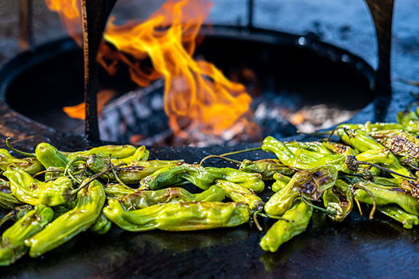 Grilled Hatch peppers with flames in the background.