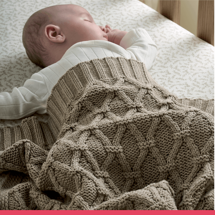 Baby sleeping peacefully under a knitted blanket in a crib.