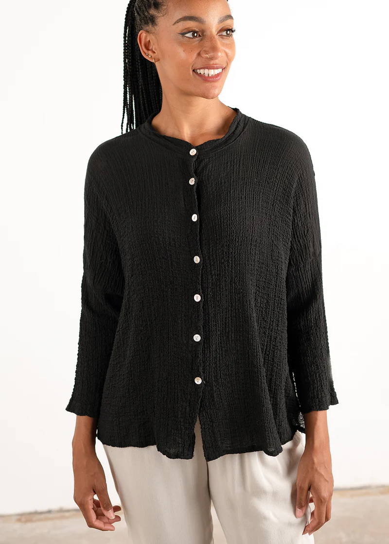 A model wearing a black, loose fitting shirt with a waffle texture and mother of pearl buttons