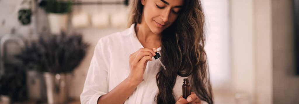 Woman with long hair holding a bottle, smiling in a bright interior setting.