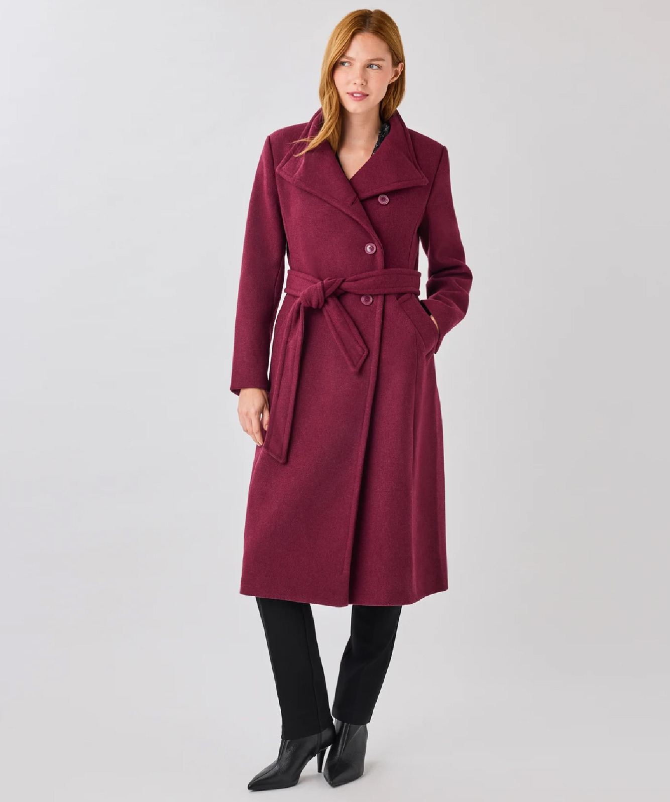 Woman wearing a burgundy coat with a belt, standing against a neutral background.