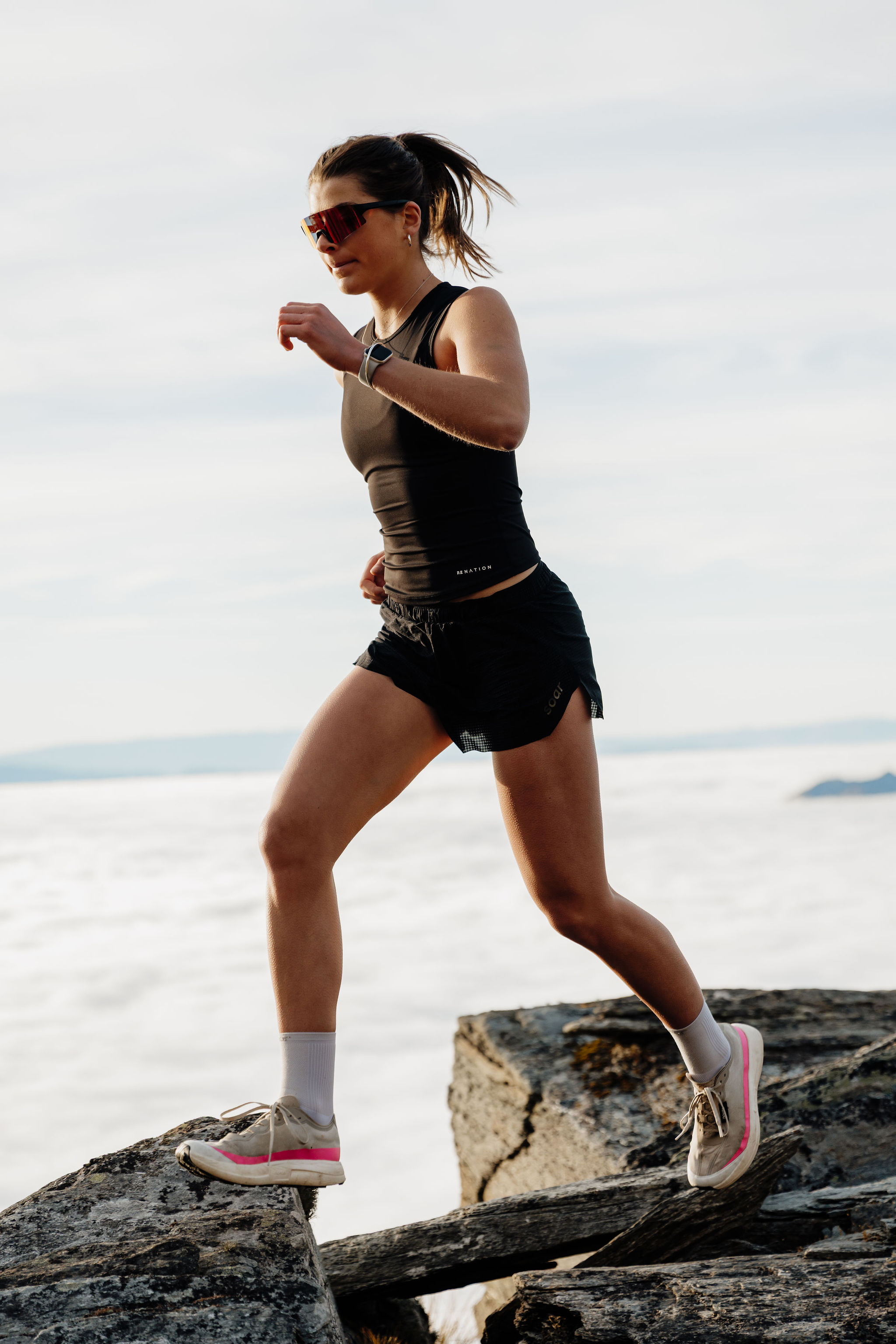 A woman running on rocky terrain above a sea of clouds.