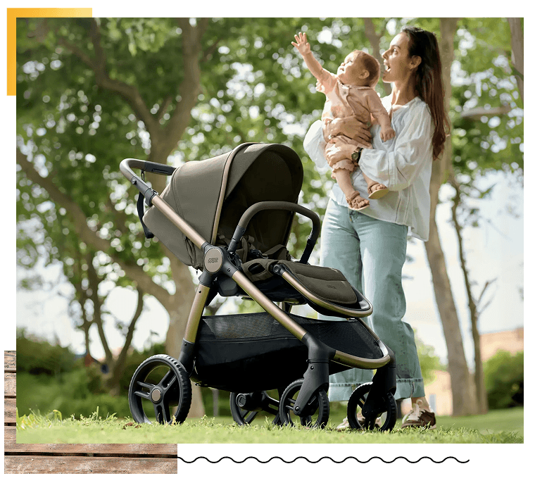 Mother holding baby beside a stroller in a park.
