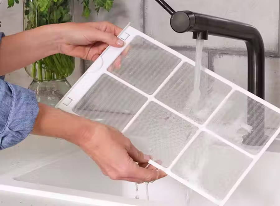 Person shown at sink washing the window AC filter.