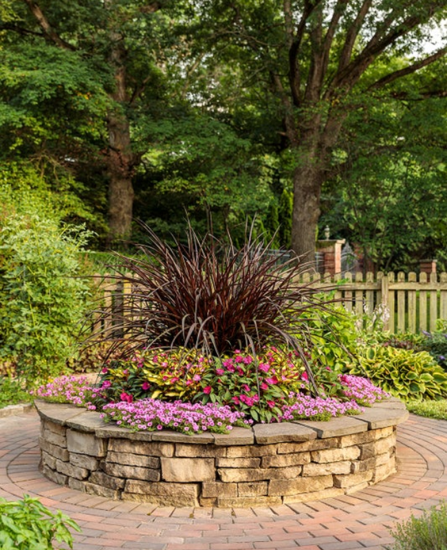 Rock garden bed planted with SunPatiens® Compact Neon Pink, Supertunia Mini Vista® Hot Pink, SunPatiens® Compact Tropical Rose, Graceful Grasses® Vertigo® 