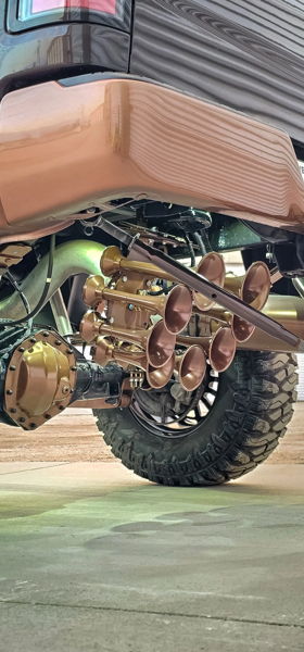 Close-up of custom bronze multi-trumpet train horn kit under rear of lifted truck with matching bronze differential cover
