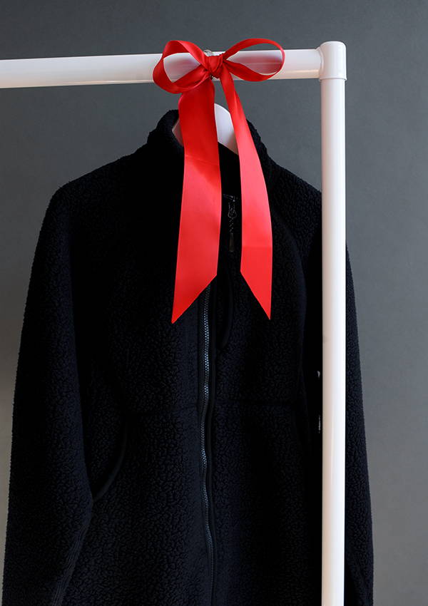 The Snow Peak Thermal Boa Fleece hung on a rail with red ribbon.