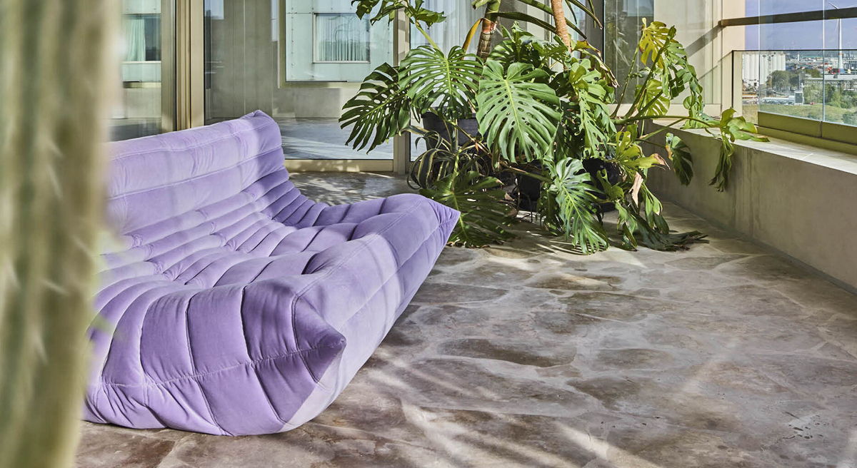 A modern purple Ligne Roset Togo beside large windows and tropical plants.