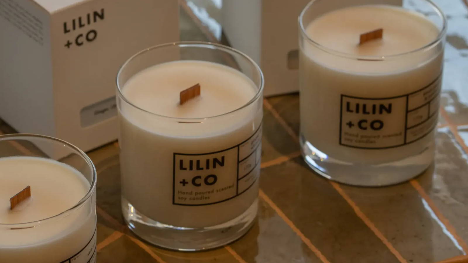 3 candles in front of their box packaging displayed on a marble counter top with 