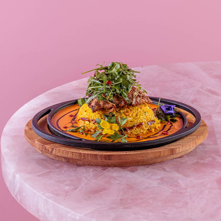 Saffron chicken risotto in a skillet on pink background
