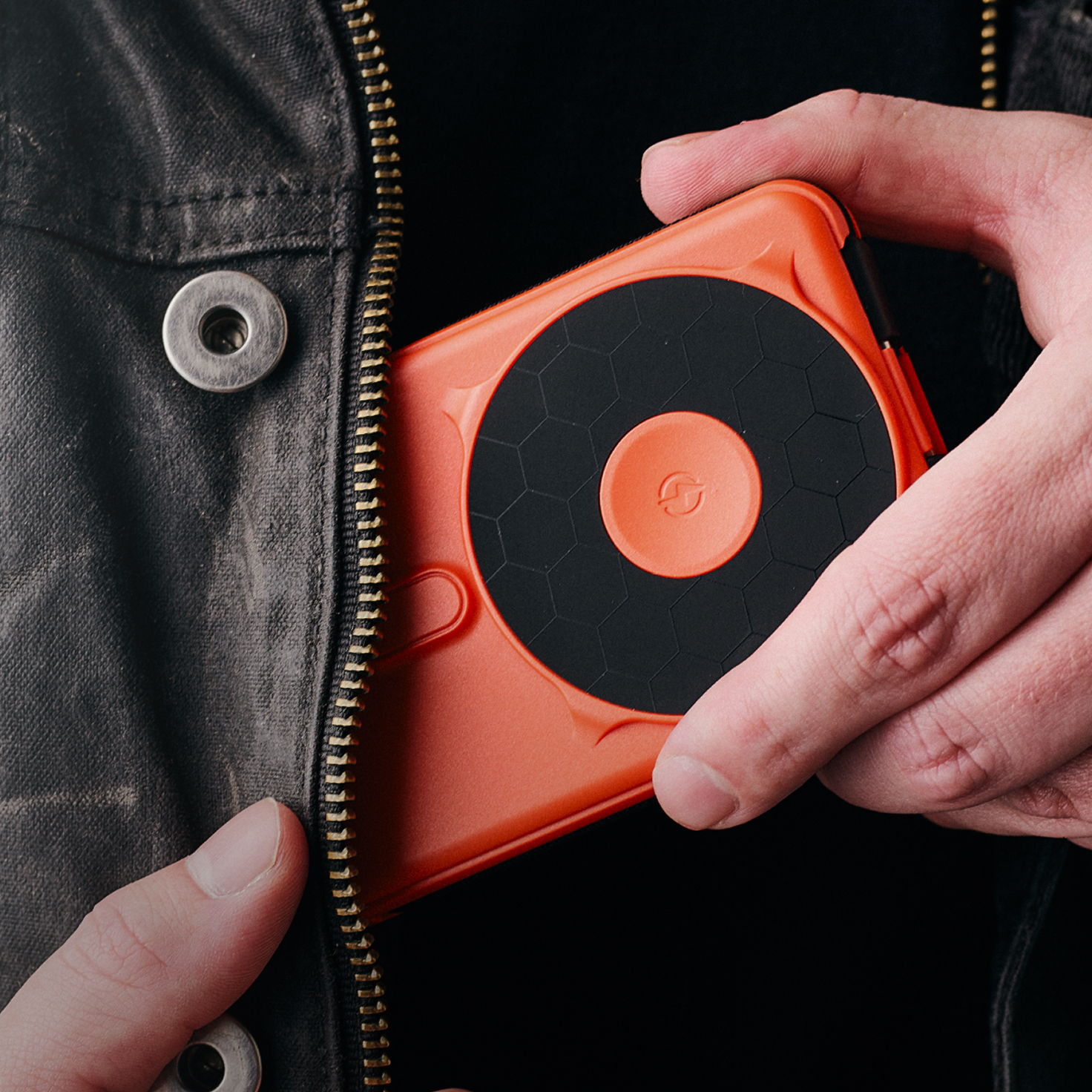 A person pulling an orange device from a jacket pocket.