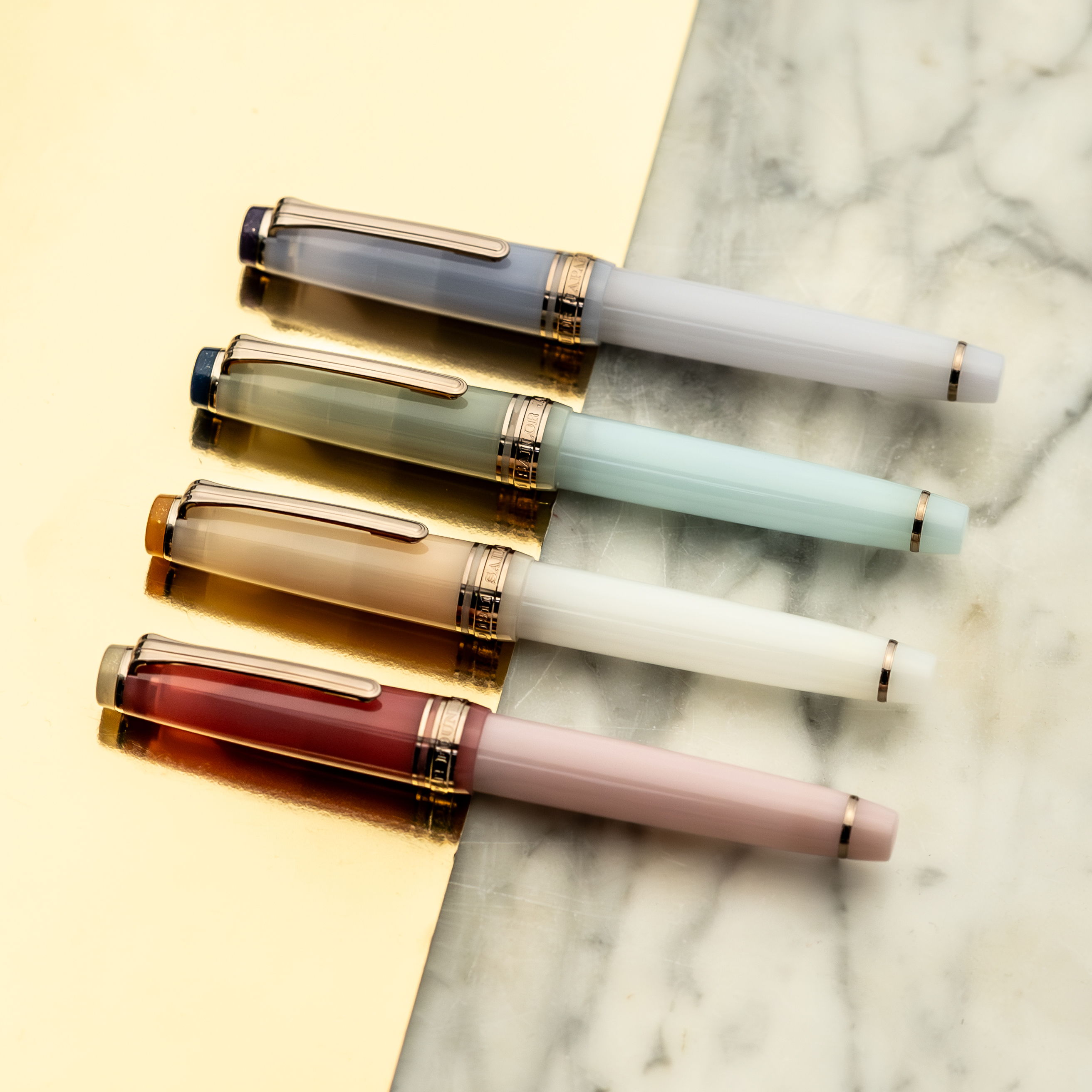 Four Sailor fountain pens resting on a gold and marble surface