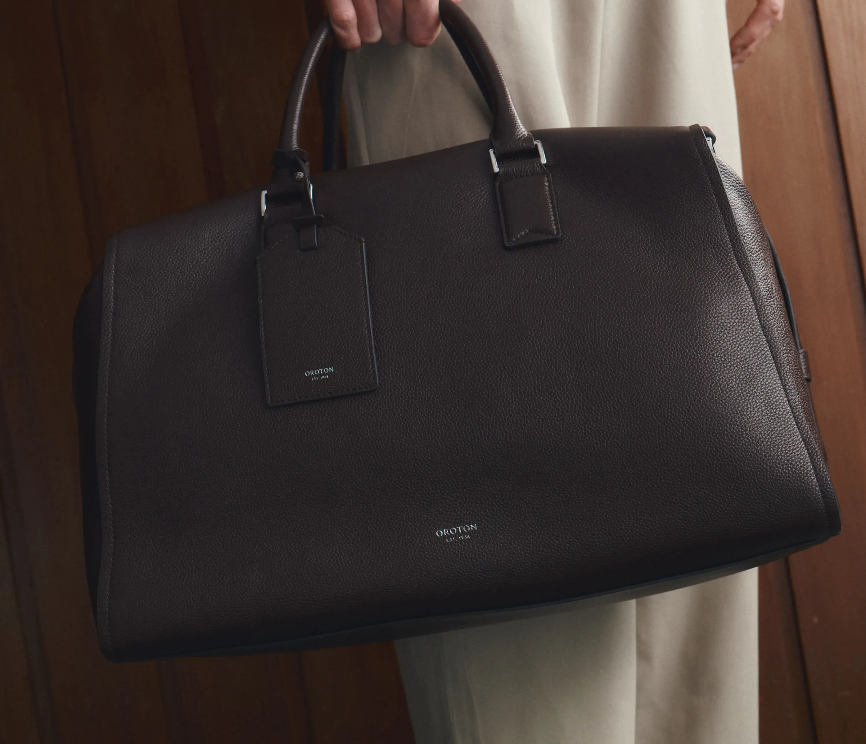 A person holding a black leather bag with a tag.
