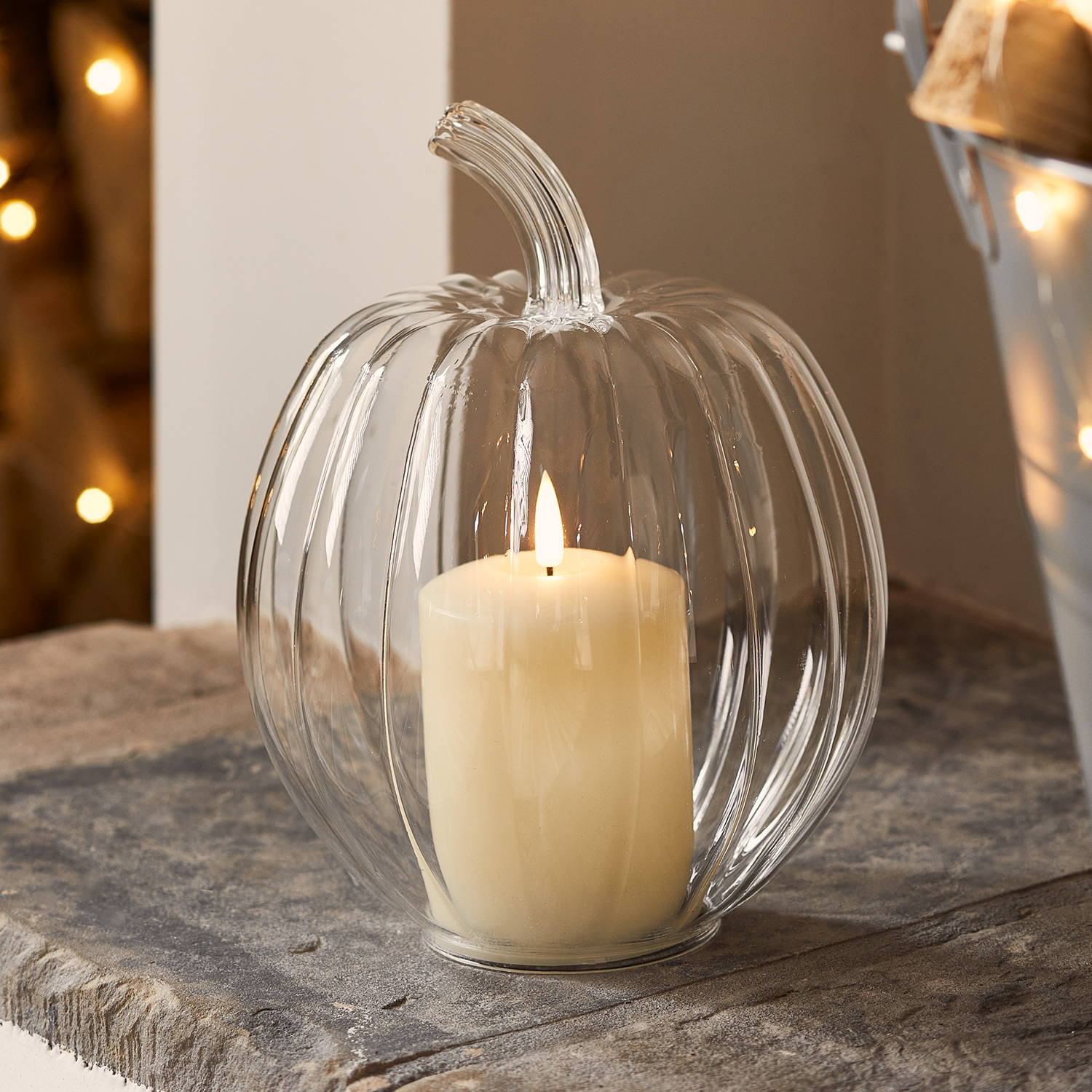 A clear glass pumpkin decoration with an ivory LED candle inside on the hearth.