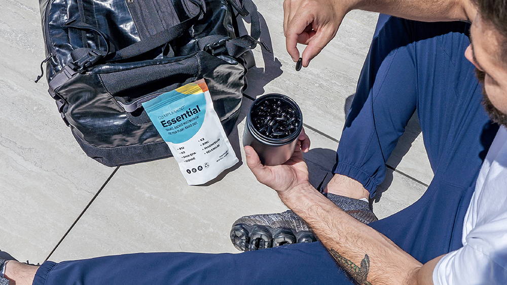 Founder Matt Tullman sitting with Complement Essential vegan multivitamin capsules and his gym bag. 