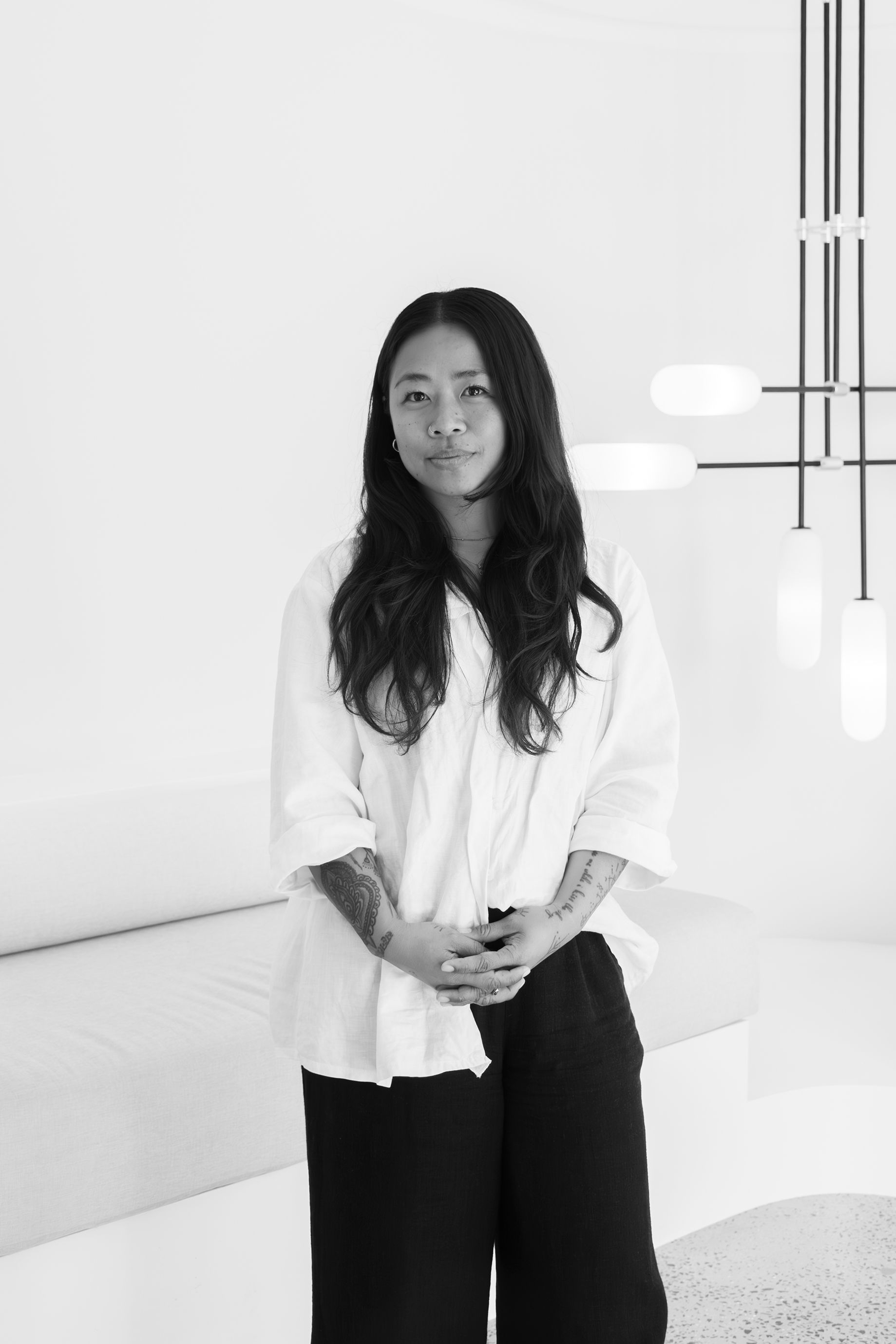 A person with long hair standing in a minimalist, white space.