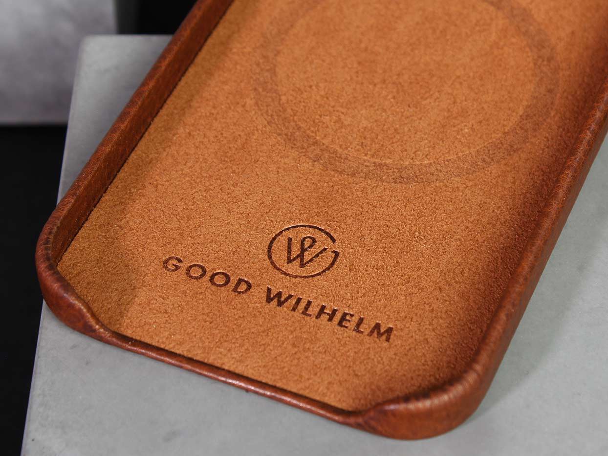 Eine iPhone Hülle in der Farbe Cognac mit dem GoodWilhelm Logo liegt auf einem Betonsockel
