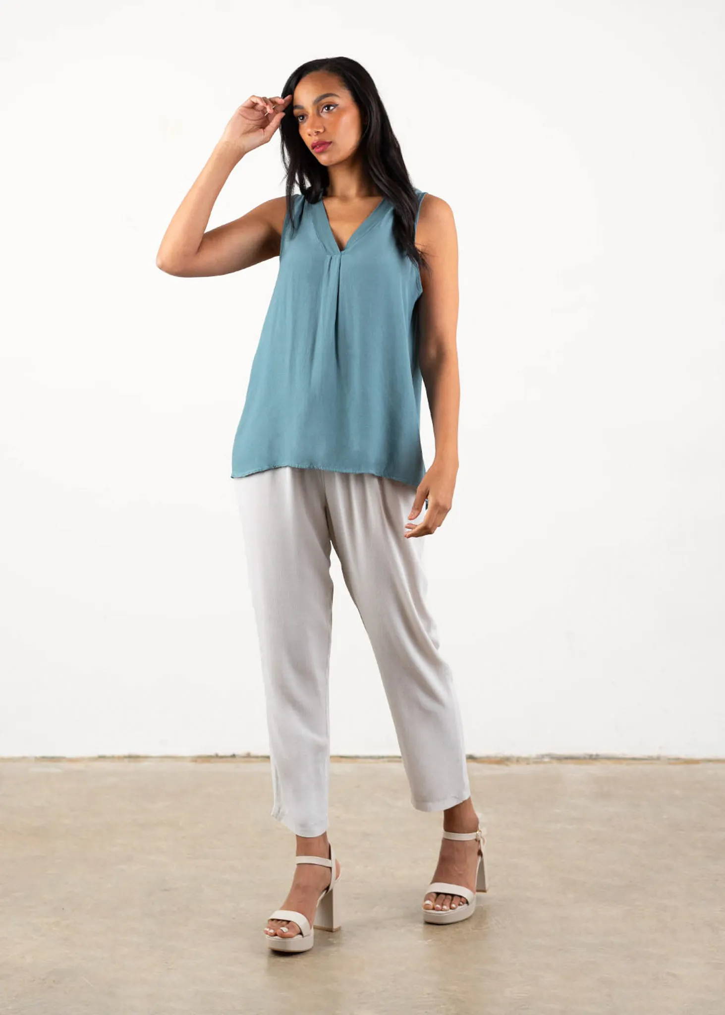 A model wearing a blue grey v neck sleeveless top with  oatmeal coloured trousers and off white heels