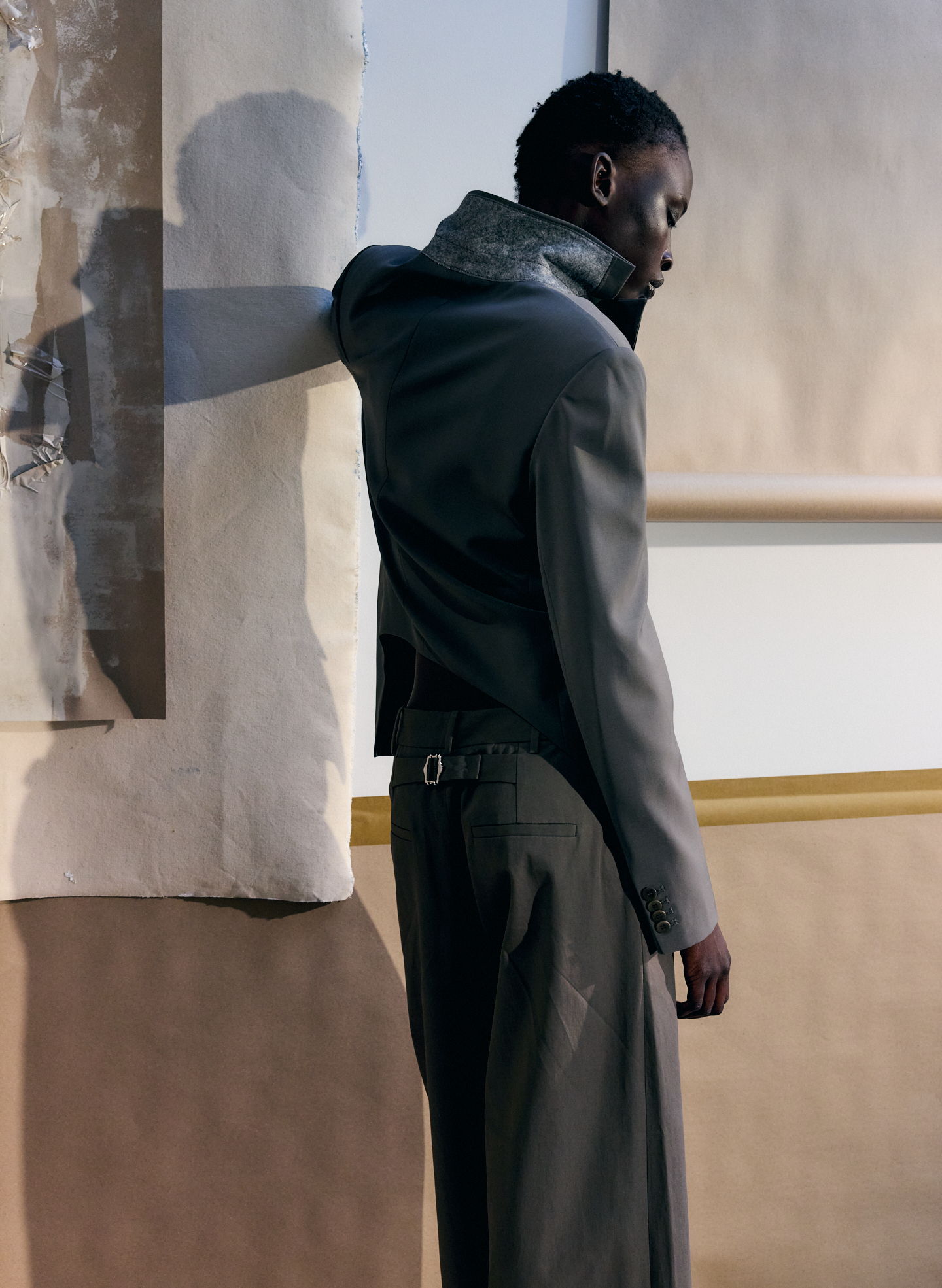 A person in a stylish outfit stands against an abstract background.