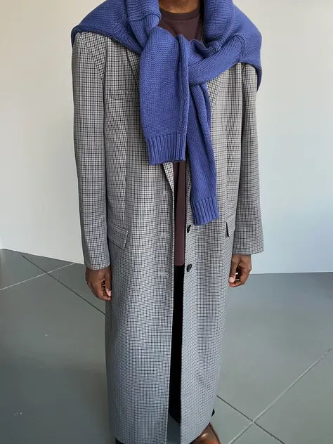 Person wearing a long coat with a blue sweater draped over shoulders.
