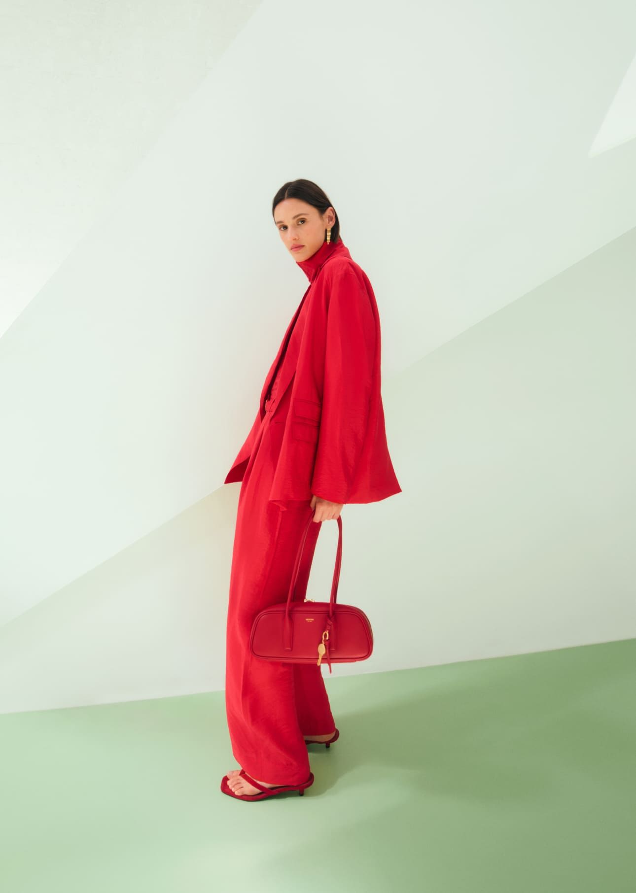 Woman in red outfit holding a red bag against a minimalist background.