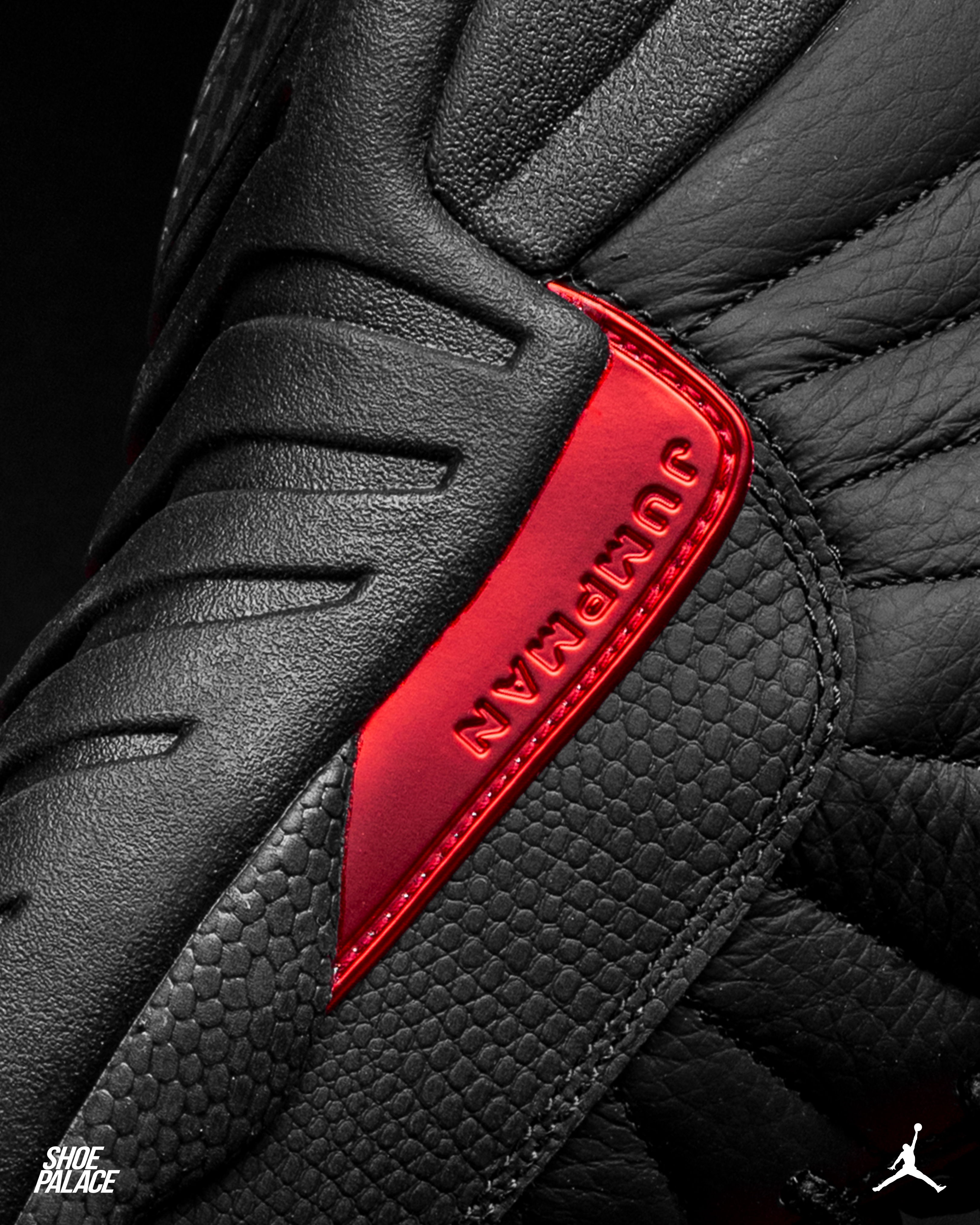 Close-up of black sneaker with red accents and textured materials.
