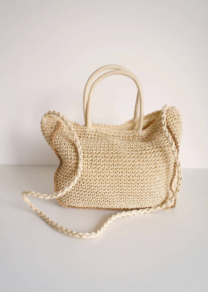 A slouchy, crochet straw shoulder bag with handles and a plaited shoulder strap