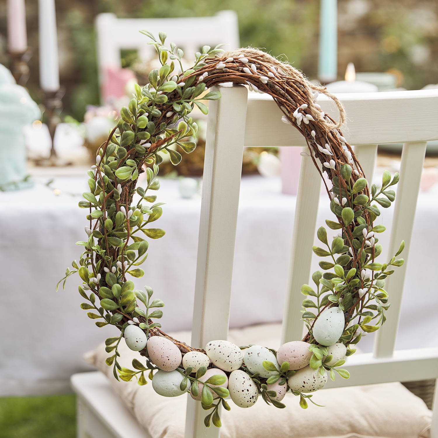 An Easter wreath with eggs and faux foliage on the back of a chair.