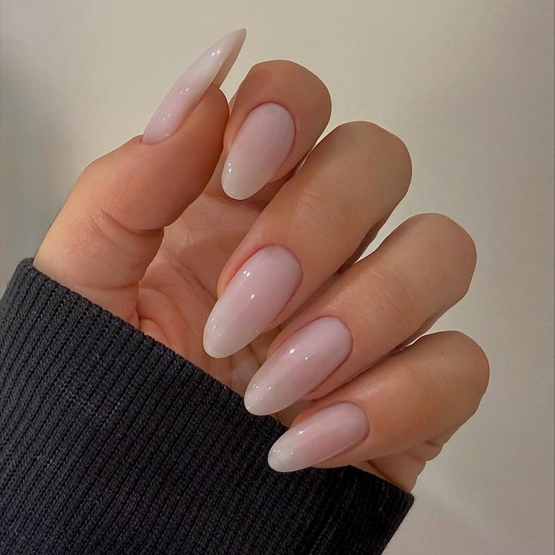 A hand with long, pink ombre nails against a dark sweater.