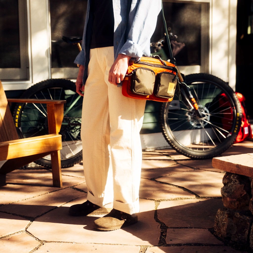 Person standing with a bag near a bicycle on a patio.