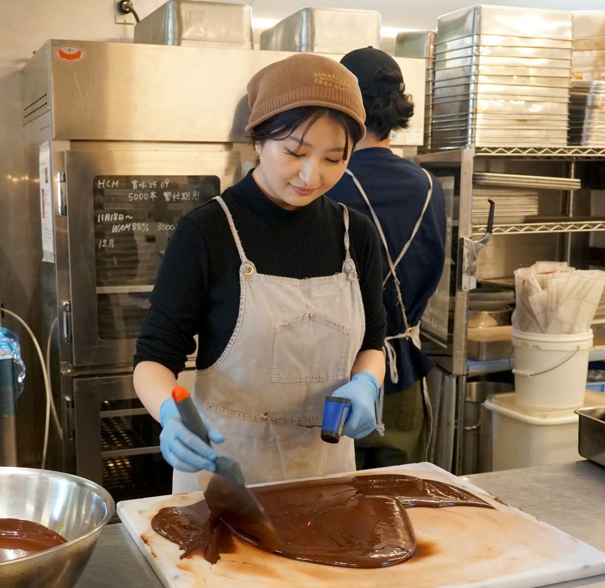 Woman in an apron spreading chocolate in a kitchen.