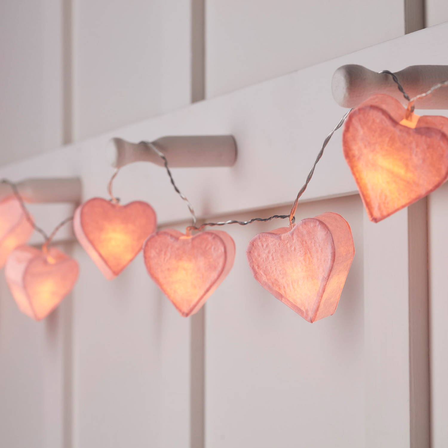 Pink paper fairy light hearts on a white wall.