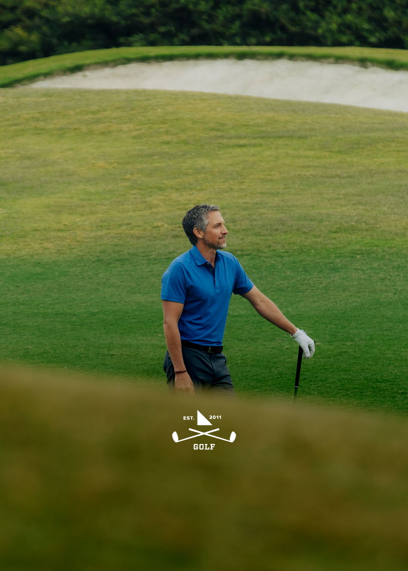 A golfer walking on the course, holding a club, wearing a blue shirt.