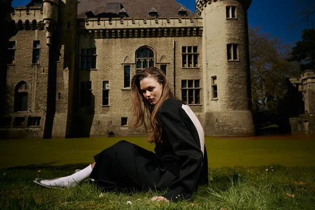 Woman in a black dress sitting on grass in front of a castle.