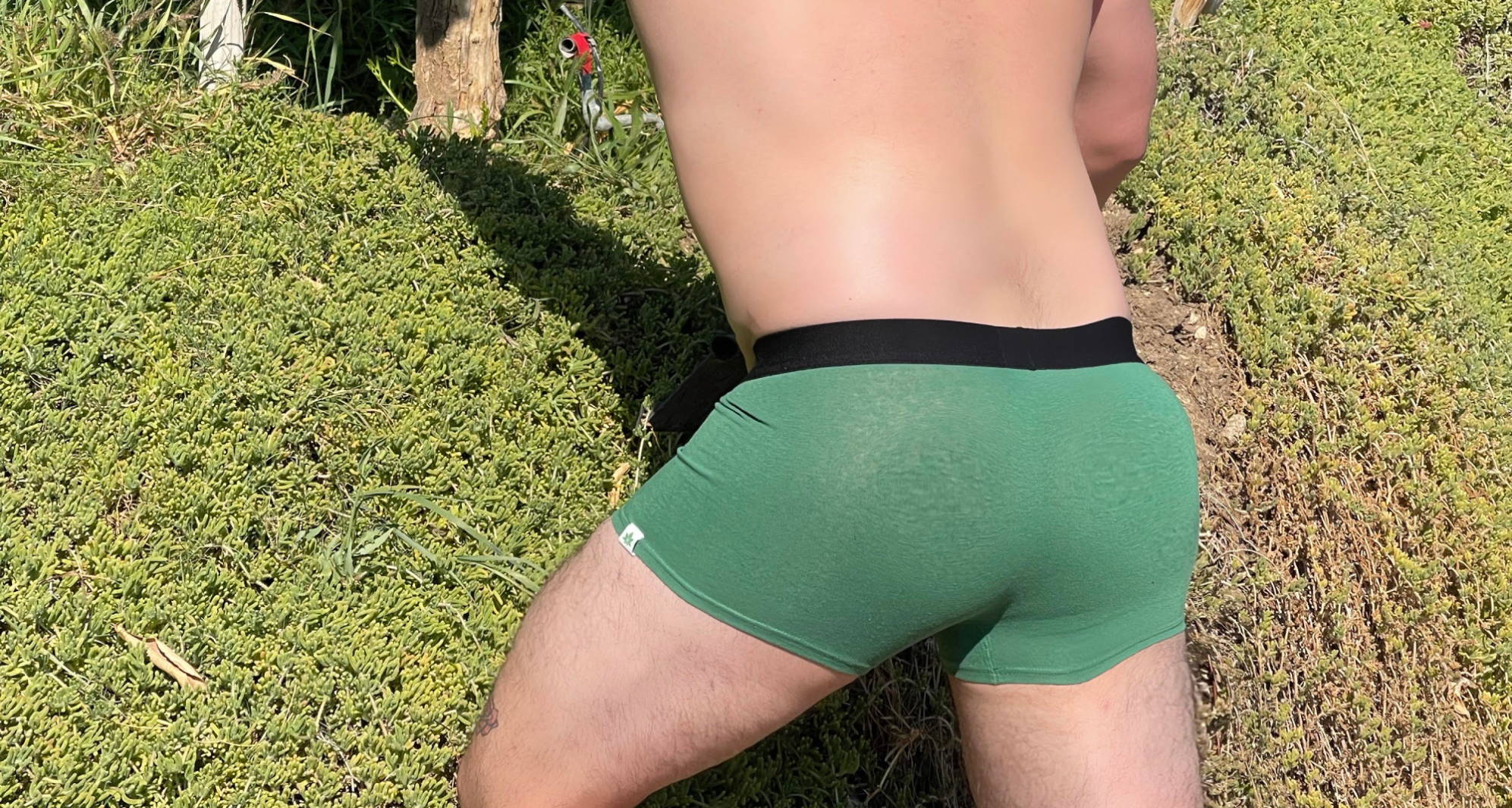 Photo from behind of a man in green trunks leaning against a mossy hill.