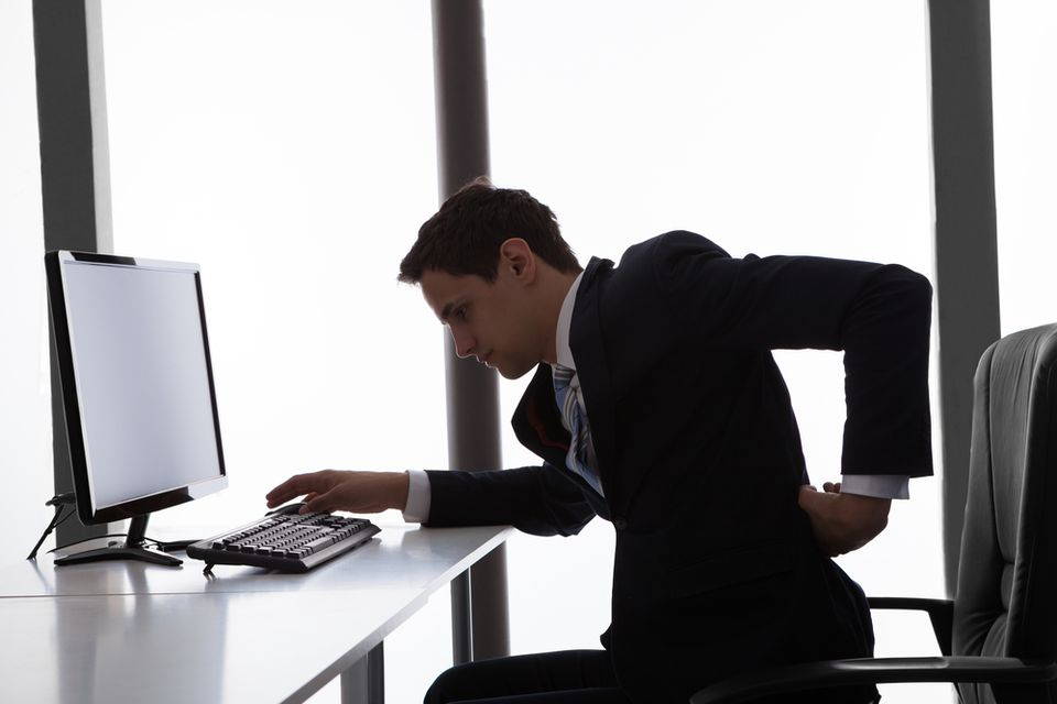 man sitting at desk touching lower back in pain