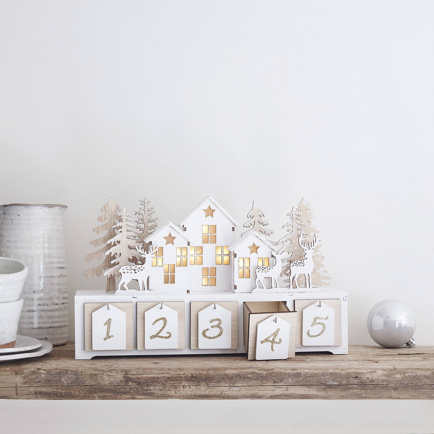 A white wooden advent calendar placed on a rustic mantlepiece 