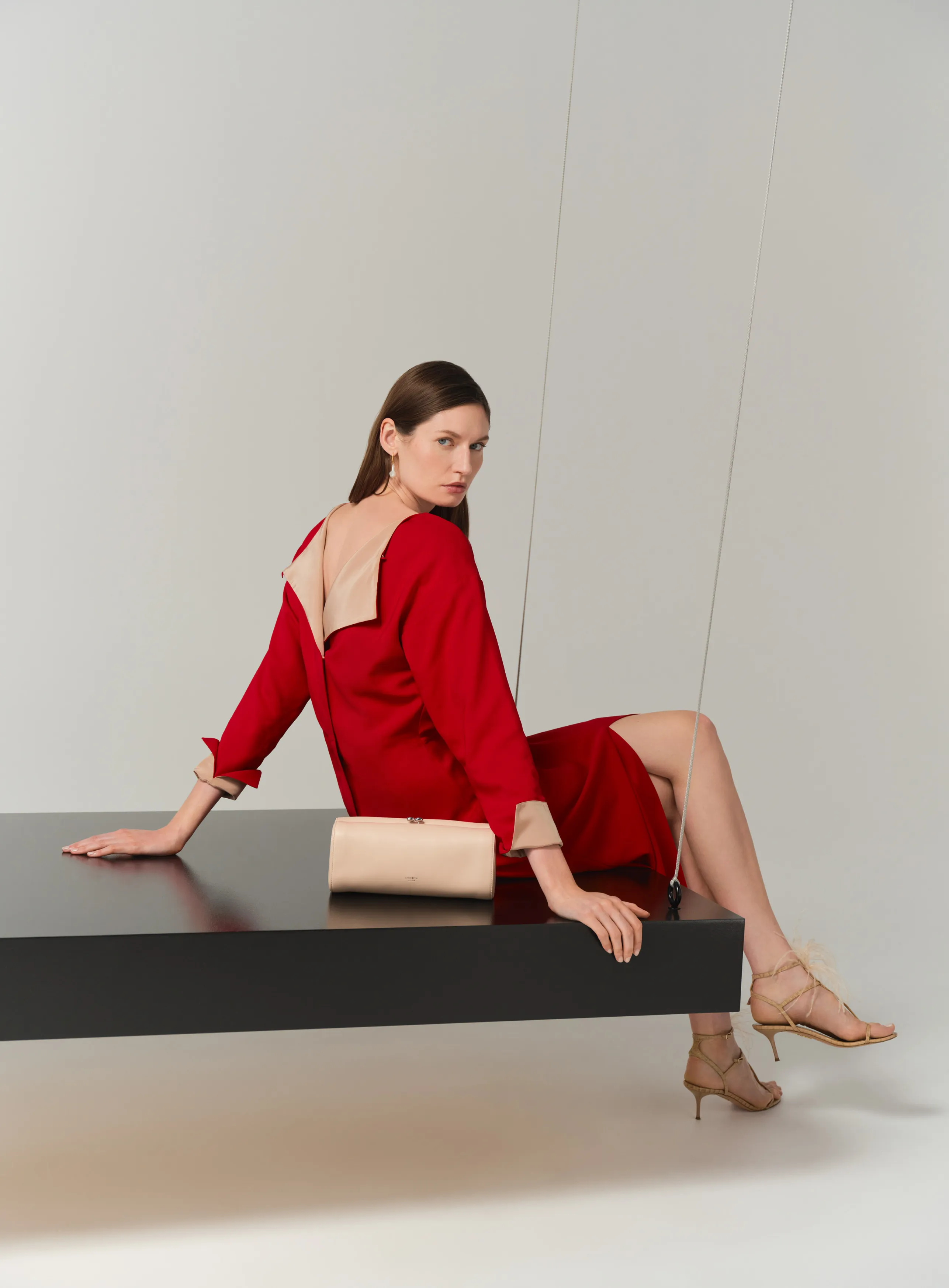 Woman in a red dress sitting on a black table with a clutch purse.