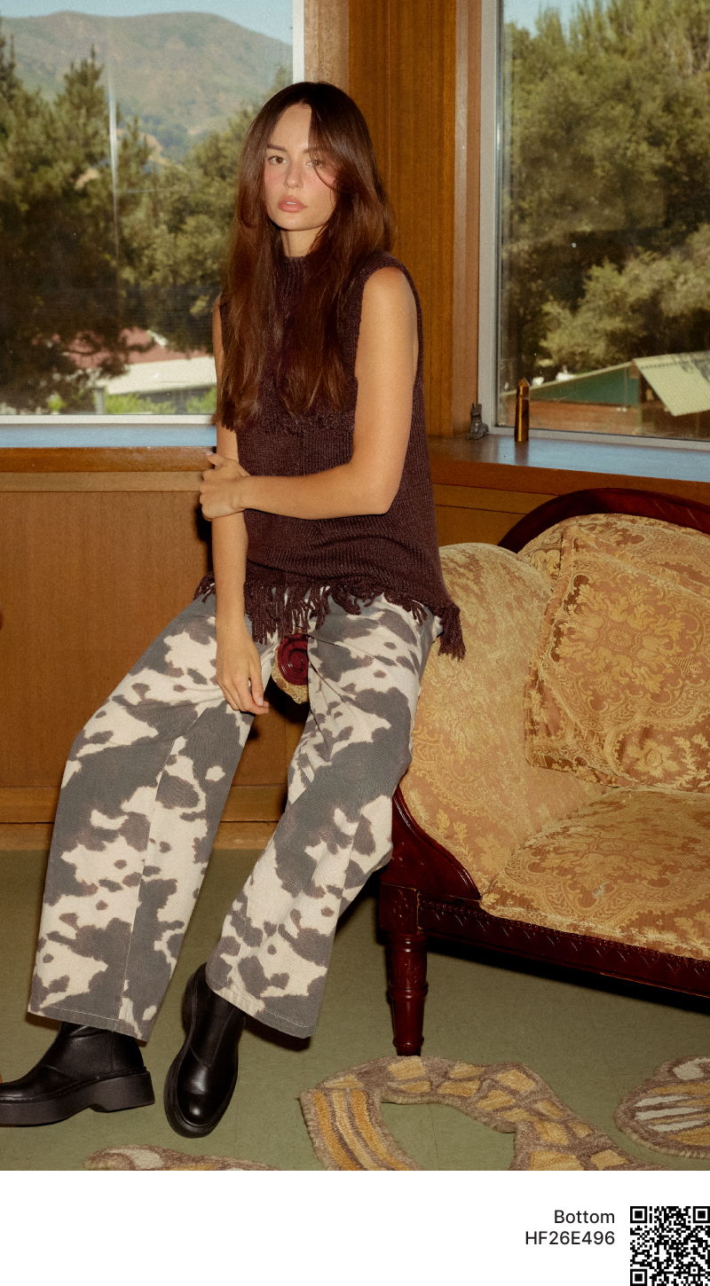 Young woman sitting on a couch, wearing a tank top and camo pants.