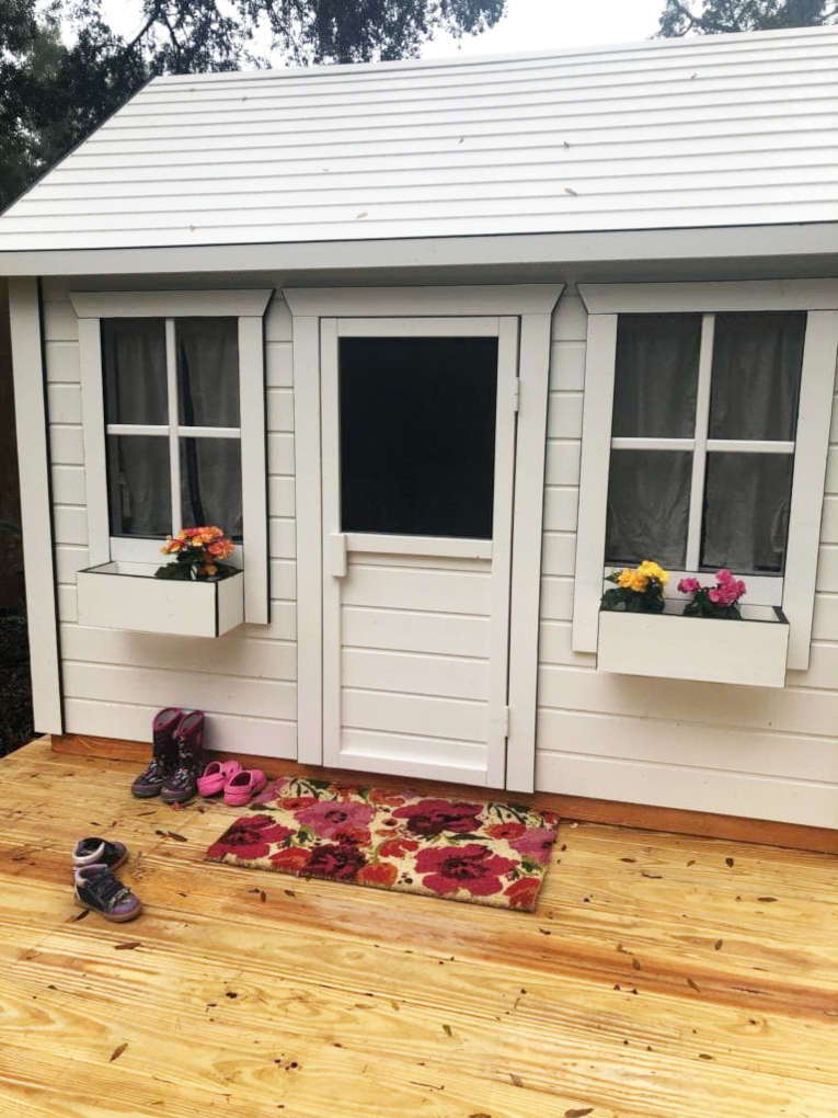 Custom Wooden Playhouse with white flower boxes and wooden terrace with floral doormat by WholeWoodPlayhouses