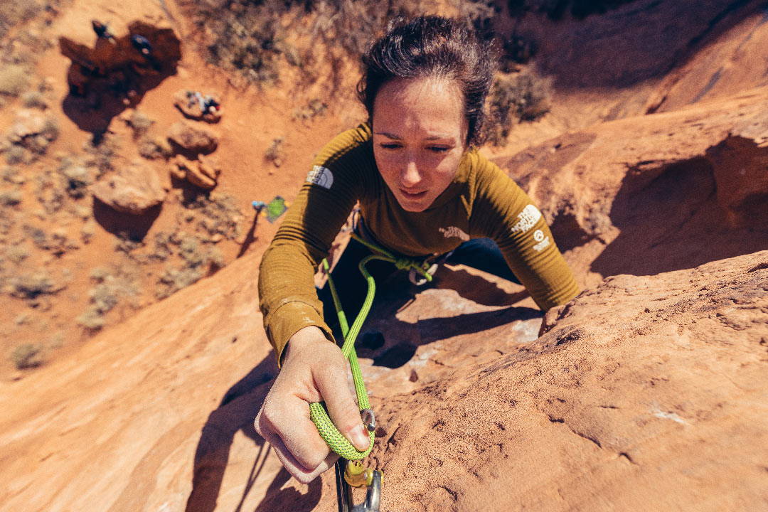 a rock climber clipping into a carabiner along a tall cliff