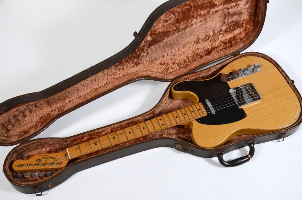 A guitar inside an open hard case with a plush interior.