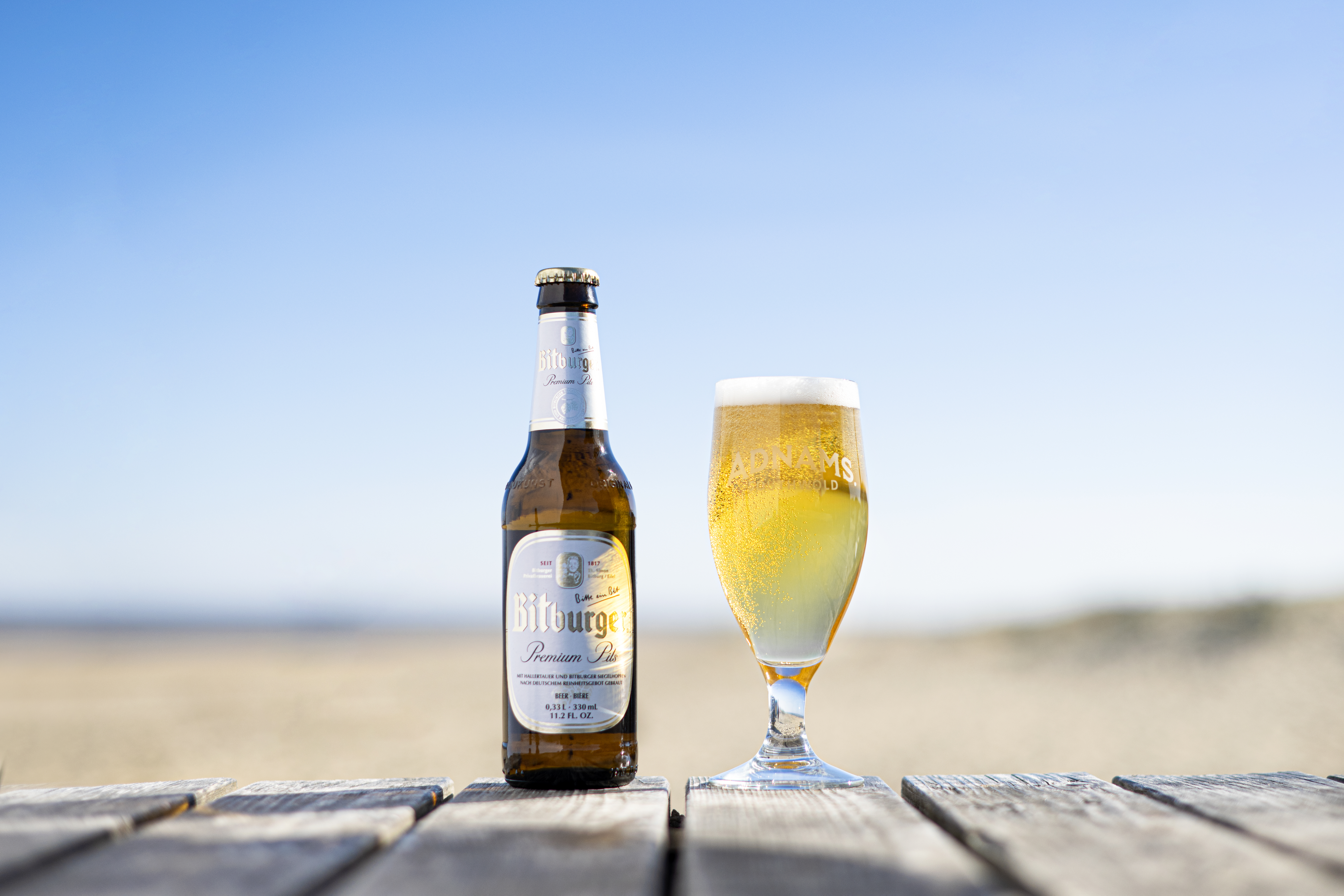 A bottle and glass of beer on a wooden table with a sunny background.
