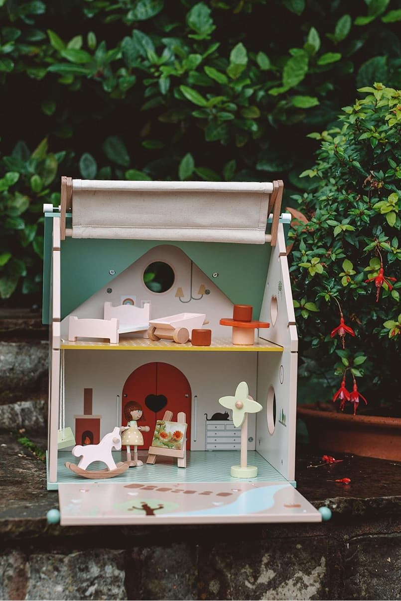 A colorful toy dollhouse with furniture and figures, surrounded by greenery.