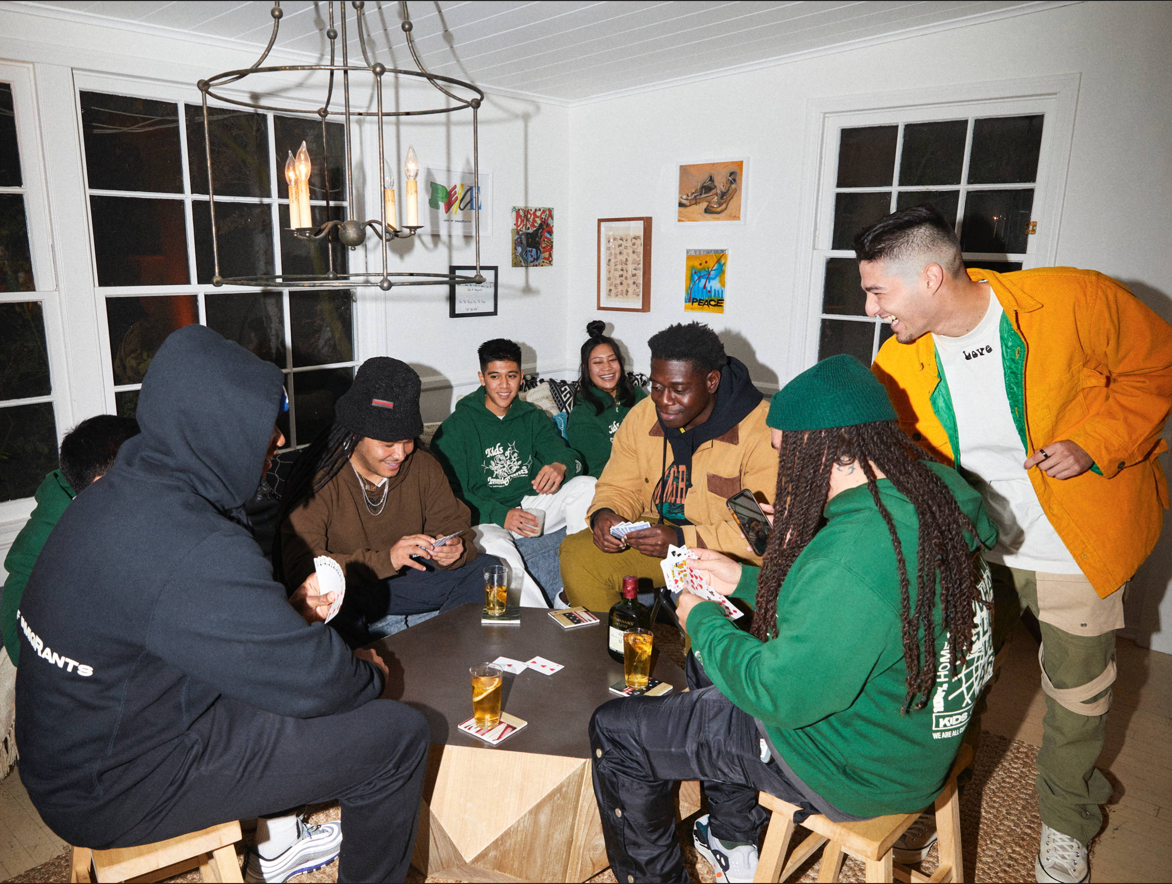 Group of people playing cards while wearing Kids of Immigrants hoodies and tees