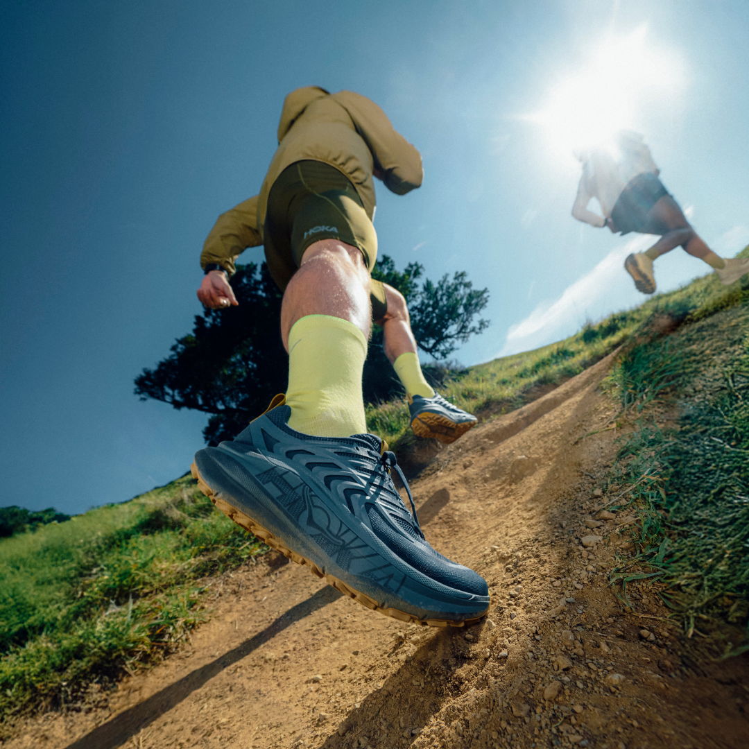 Person hiking on a trail wearing shorts and colorful socks, sunlight overhead.