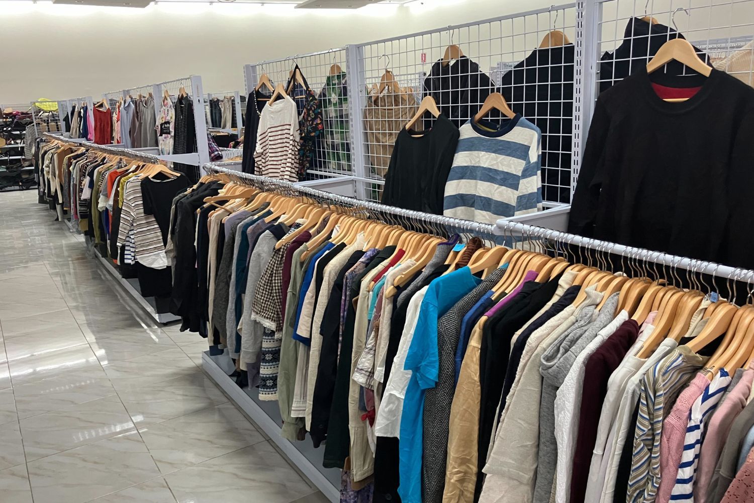Clothing racks displaying various shirts and sweaters in a retail store.
