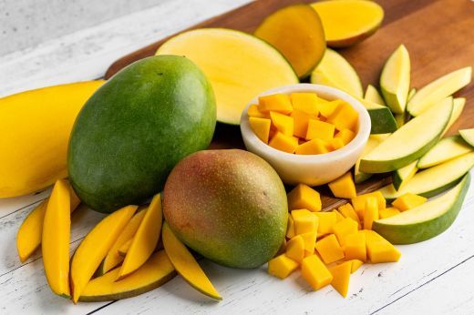 A variety of fresh mangoes and cut mango pieces on a wooden surface.