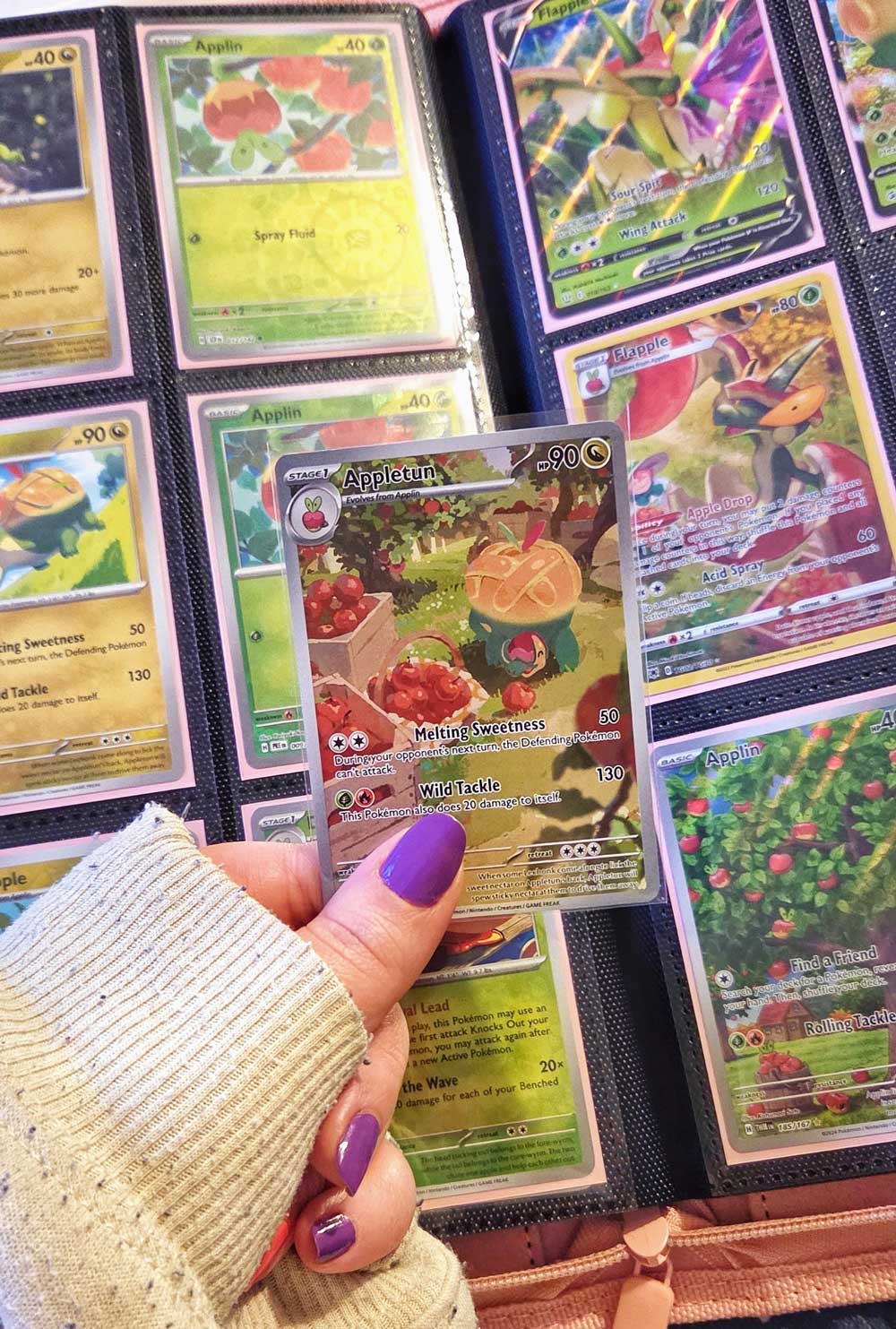 Person holding a Pokémon card above a collection of cards in a binder.