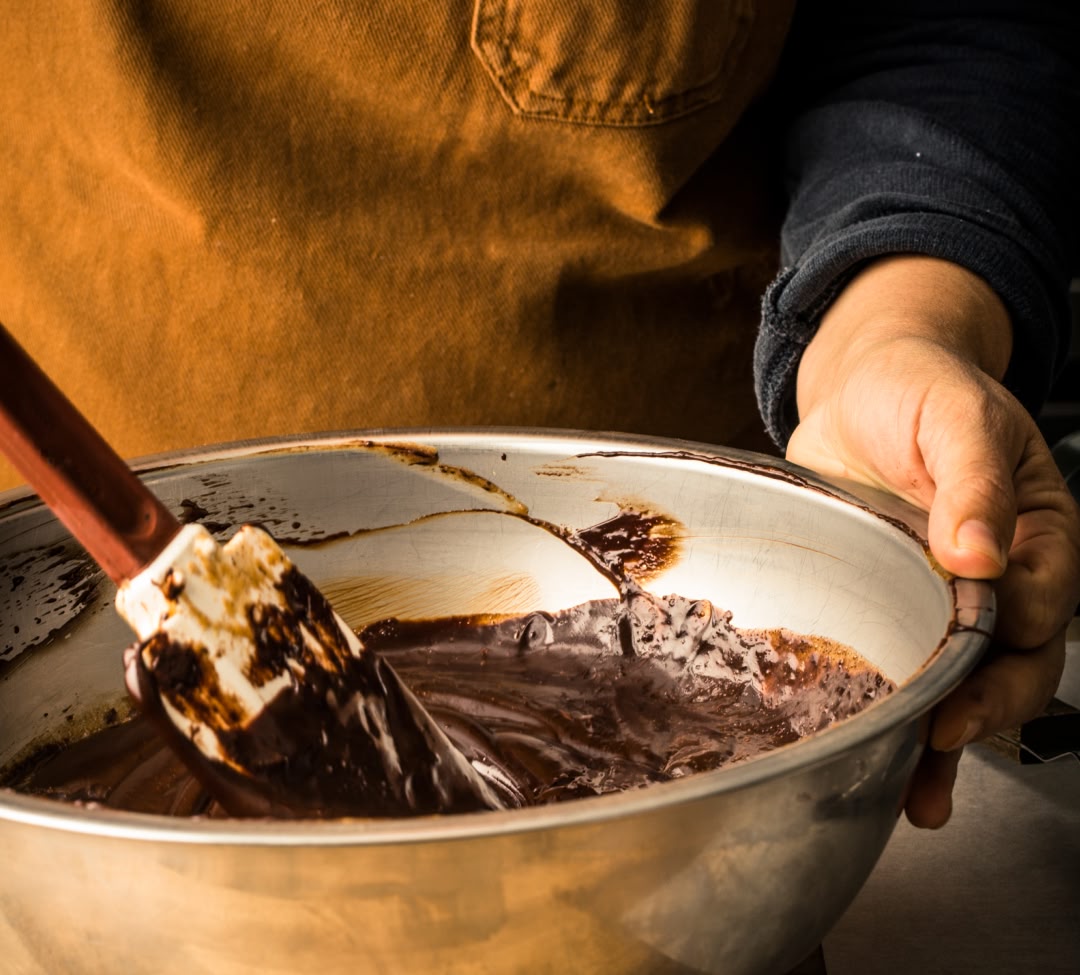 Person mixing chocolate batter in a bowl with a spatula.